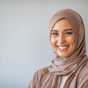 Portrait of a young woman in traditional Muslim clothing, smiling. Beautiful woman headshot looking at camera and wearing a hijab. Arabian woman with happy smile. Strict formal outfit and elegant appearance. Islamic fashion.